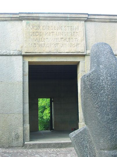 Ein monumentales Denkmal mit einer steinernen Inschrift. Auf der rechten Seite steht eine skulpturale Darstellung.