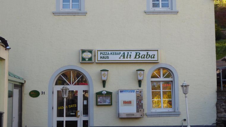 A restaurant named "Ali Baba" is visible on a bright building facade. The windows are oval, and the entrance door invites entry.