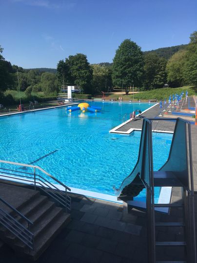 Ein Schwimmbad mit klarem blauem Wasser und einem Rutschenbereich. Umgeben von Bäumen und einer schönen Landschaft.