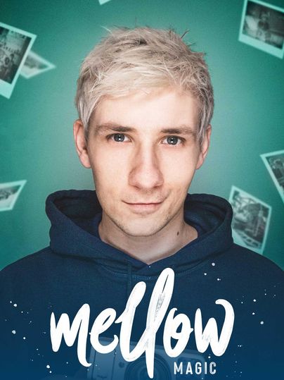 Een jonge man met blond, kort haar draagt een blauwe hoodie. Achter hem zijn zwart-witte foto's op een groene muur gerangschikt.