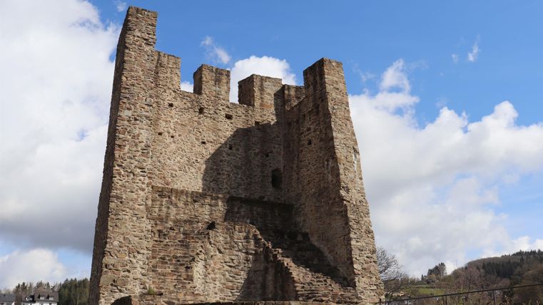 Un ancien château avec de grandes tours et une façade partiellement écaillée. Le ciel est bleu avec quelques nuages.