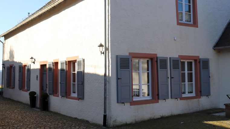 A charming house with white walls and colorful shutters. The sunny atmosphere and the paved path give the place an inviting character.