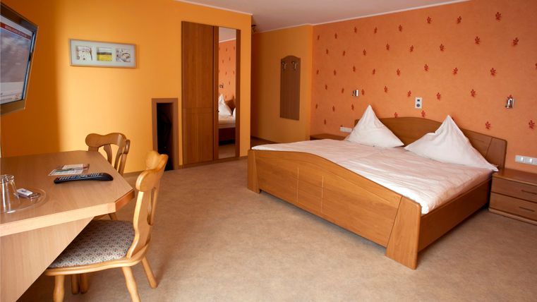 A cozy hotel room with a large bed and a desk. The walls are painted in a warm orange, and there is a television.