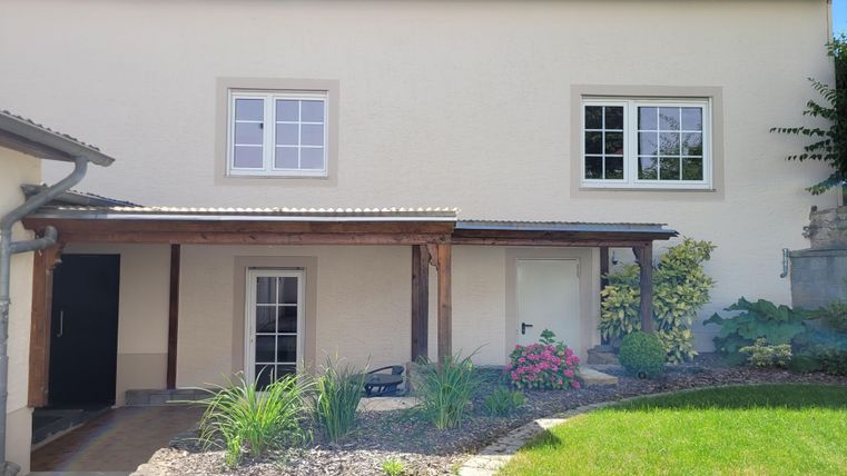 A modern house with a well-maintained garden and beautiful plants. The entrance is covered, and the windows are bright and inviting.
