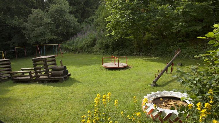 A playground with various play equipment in a green park. The surroundings are filled with trees and flowers.
