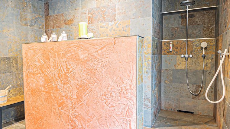 A modern shower area with an orange wall and fine stone tiles. The atmosphere is bright and inviting.