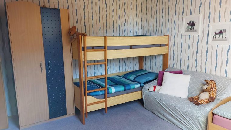 A cozy children's room with a loft bed and a sofa. The walls are decorated with colorful patterns, and there are some pictures of animals.