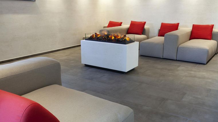 A modern living room with cozy sofas and red cushions. In the center, there is an elegant table with a fireplace.