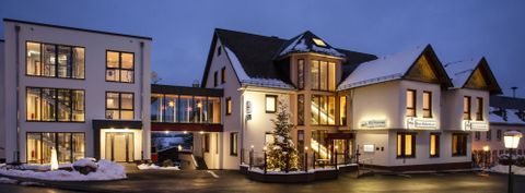 Ein modernes Hotelgebäude mit warmem Licht und Schneebedecktem Boden. Es ist Nacht und die Architektur ist einladend.