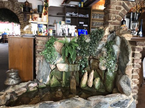 A small waterfall with stones and plants in a restaurant. The surroundings are cozy and inviting.