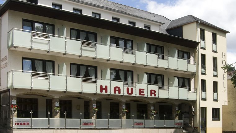 Ein modernes Hotelgebäude mit mehreren Balkonen. Die Fassade ist hell und einladend, mit dem Schriftzug "HAUER" gut sichtbar.