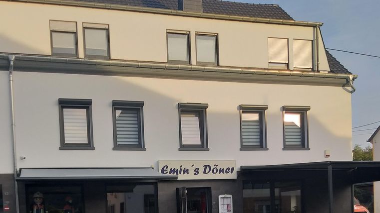Een restaurant genaamd "Emin's Döner" in een modern gebouw. De gevel is licht, met ramen en een overdekt buitengedeelte.