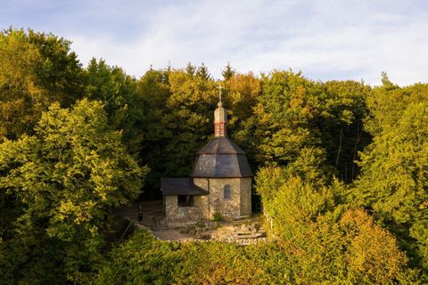 Eine kleine Kirche umgeben von buntem Herbstwald. Die Landschaft ist ruhig und malerisch.