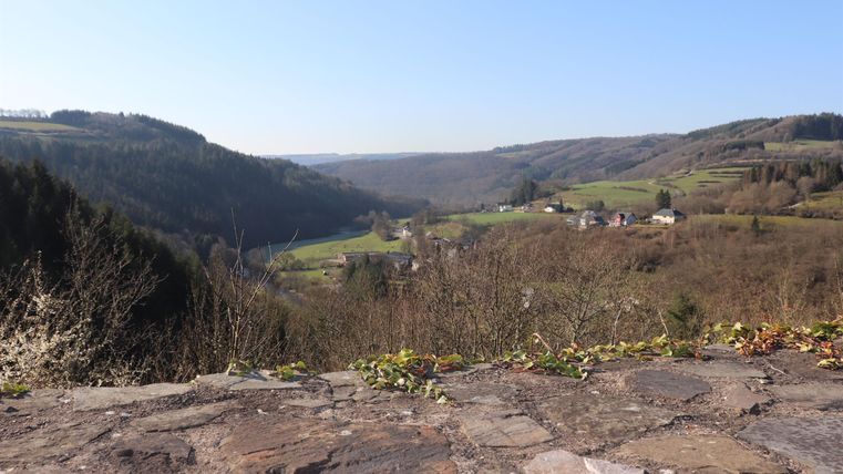 A picturesque valley with gentle hills and a clear blue sky. In the background, some buildings can be seen in the tranquil landscape.