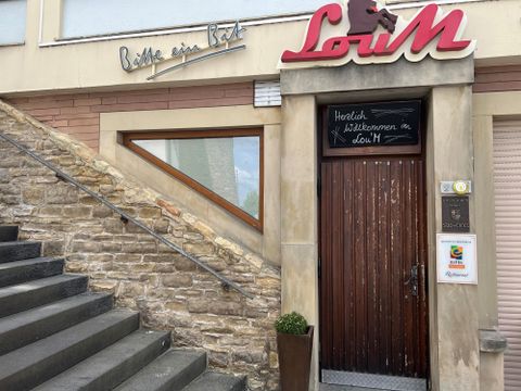 Une entrée à un restaurant confortable avec un portail en bois. Au-dessus de la porte, il est écrit "Bienvenue au LöM".