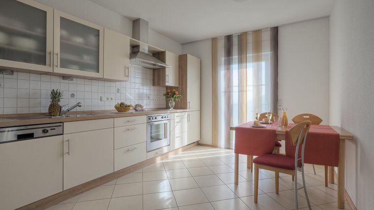 Eine moderne Küche mit hellem Interieur und einer kleinen Essgelegenheit. Licht fällt durch das Fenster und schafft eine einladende Atmosphäre.