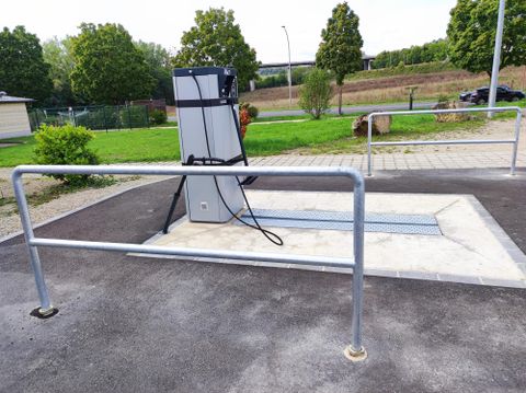 Een modern tankstation met een pomp en een slang. Het gebied is schoon en omgeven door groene natuur.