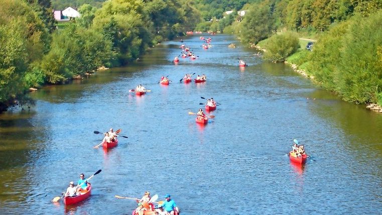 A picturesque river landscape with many red canoes. People are enjoying an exciting day paddling in nature.