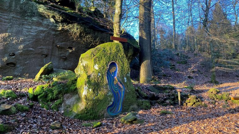 Une roche colorée avec une représentation artistique dans une forêt. Entourée de feuillage et de grands arbres sous la lumière du soleil.