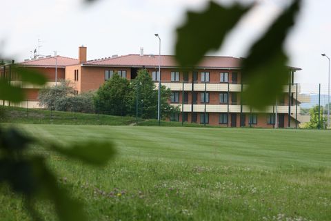 Een modern gebouw met meerdere verdiepingen staat in een groene omgeving. Omgeven door weilanden en bomen lijkt het uitnodigend en rustgevend.