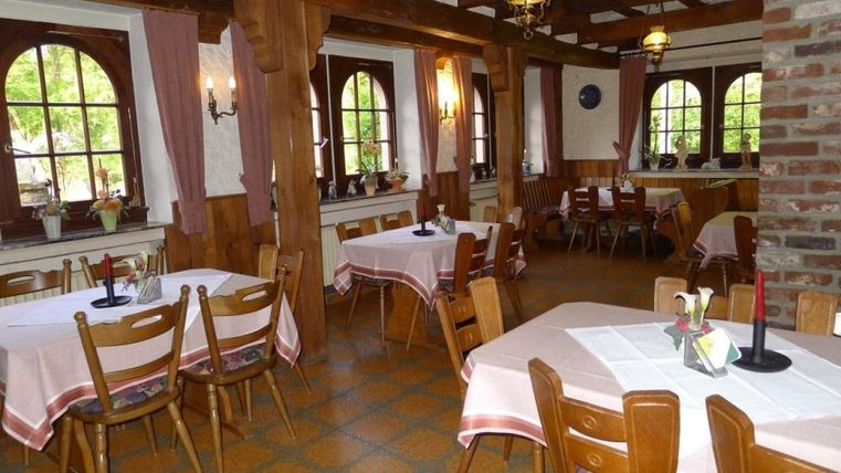 A cozy restaurant with wooden furniture and white tablecloths. The large windows provide plenty of daylight and an inviting atmosphere.