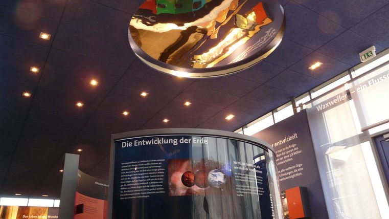 A modern exhibition space with interactive panels on Earth history. The ceiling reflects light and showcases a fascinating design.