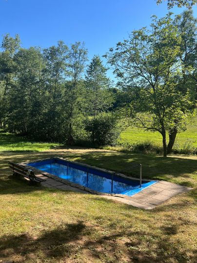 Ein schöner Swimmingpool inmitten von Grünflächen und Bäumen. Der Himmel ist klar und blau, ideal für einen entspannten Tag im Freien.