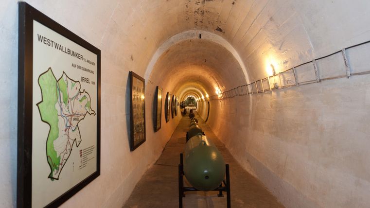 A long, bright tunnel with drawn maps on the walls. In the center, there are historical military objects that emphasize the cool character of the space.
