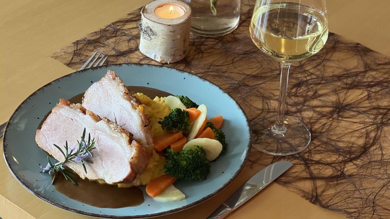 A plate with juicy meat, vegetables, and mashed potatoes. Next to it, there is a glass of white wine on an elegant table.