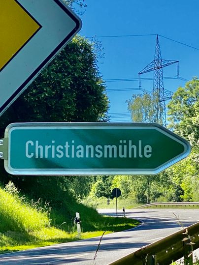 Een verkeersbord wijst de richting naar Christiansmühle. Op de achtergrond zijn bomen en een blauwe lucht zichtbaar.