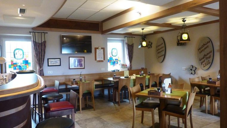 Ein einladendes Restaurant mit Holzmöbeln und warmem Licht. Es gibt Tische mit Stühlen und eine Bar in einem gemütlichen Ambiente.