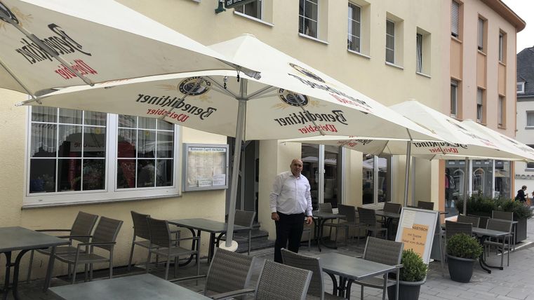 A cozy restaurant with an outdoor terrace and sun umbrellas. A waiter is ready to welcome the guests.
