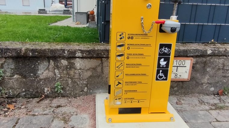 Een gele reparatiestation voor fietsen staat op een trottoir. Het bevat verschillende gebruiksaanwijzingen en is gemakkelijk toegankelijk.