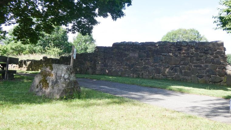 An old stone wall in a green park. The path runs along the wall under the shade of the trees.