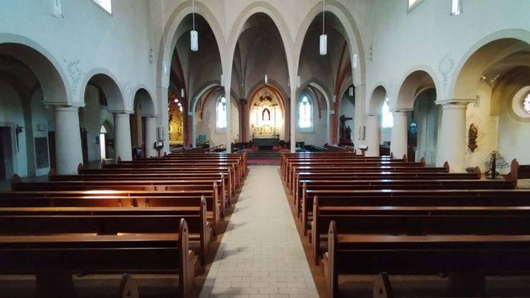 Een rustige kerk met houten bankrijen en hoge, gewelfde plafonds. Op de achtergrond is een altaar te zien.
