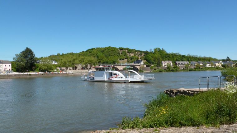 Een schip vaart op een rustige rivier, omgeven door groene heuvels. De lucht is helder en blauw.