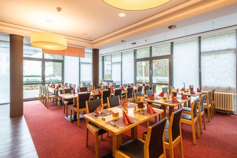 Een modern restaurant met houten stoelen en tafels. De inrichting is helder en uitnodigend, met grote ramen waar daglicht binnenstroomt.