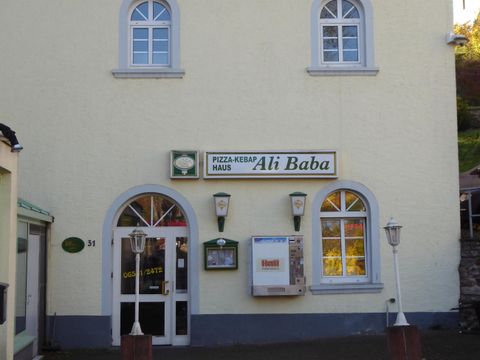 A restaurant named "Ali Baba" is visible on a bright building facade. The windows are oval, and the entrance door invites entry.