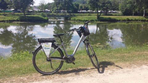 Une balade à vélo dans la nature avec un VTT électrique, qui se trouve près d'un lac paisible. En arrière-plan, on peut voir des arbres et un terrain de camping.