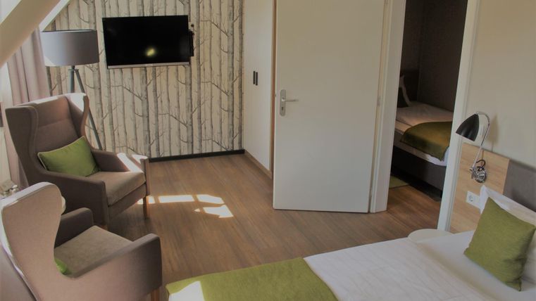 A modern hotel room with two comfortable chairs and a television on the wall. The rooms are bright and friendly furnished, with green accents.