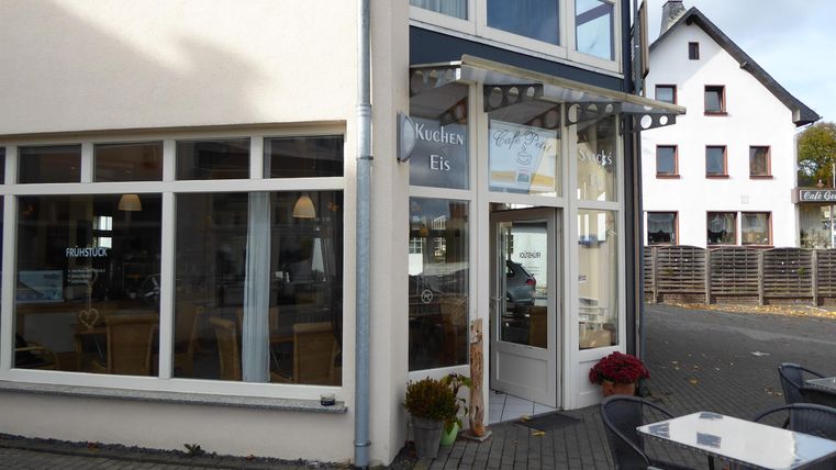 Een mooi café aan een rustige straat met grote ramen. Buiten staan er tafels en stoelen voor gasten.