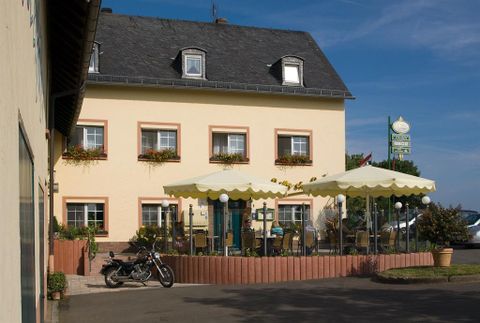 Une auberge confortable avec des fenêtres fleuries et une terrasse. Dehors, il y a une moto et des parasols pour se détendre.