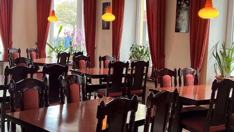 Een gezellig restaurant met houten stoelen en tafels. De warme kleuren van de gordijnen en lampen creëren een uitnodigende sfeer.