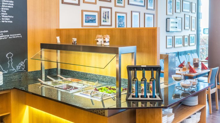 Een licht restaurant met een buffet en een grote verscheidenheid aan gerechten. Aan de muren hangen foto's, en er zijn gezellige zitgelegenheden.