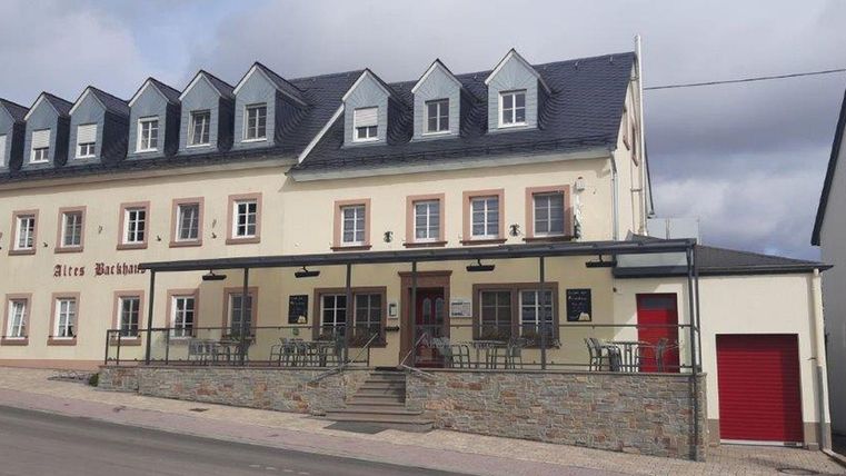 Een charmant hotel met twee verdiepingen en een hoog dak. De gevel is licht en uitnodigend, met zitgelegenheden buiten.