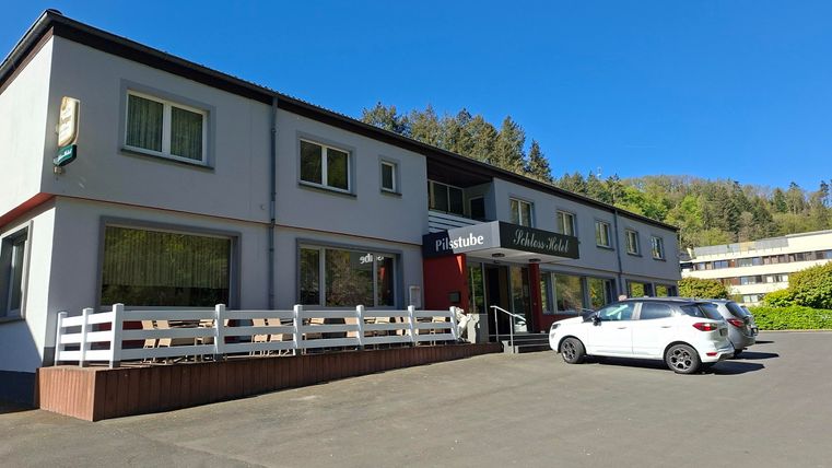 A small inn with a bright facade and an inviting entrance area. Several cars are parked in front of the building.