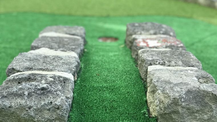 A small stone path on green artificial grass. In the background, a round stone border is visible.