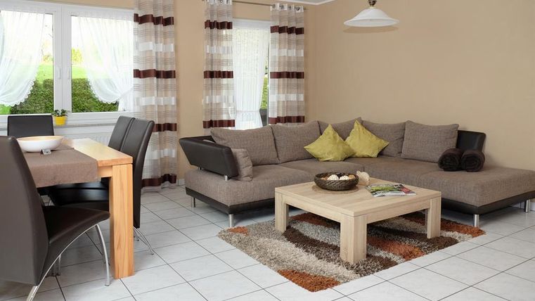 A modern living room with a comfortable L-shaped couch and a wooden table. Large windows let in plenty of daylight and create an inviting atmosphere.