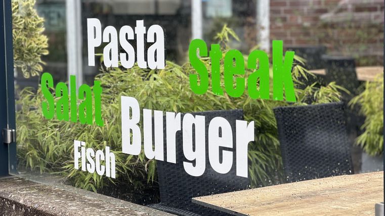 Een restaurantraam met een menukaart. Er staan verschillende gerechten op afgebeeld zoals pasta, steak, salade, vis en burger.