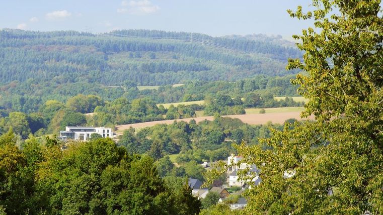 A picturesque landscape with gentle hills and lush green. In the foreground, trees can be seen, while a beautiful valley stretches out in the background.